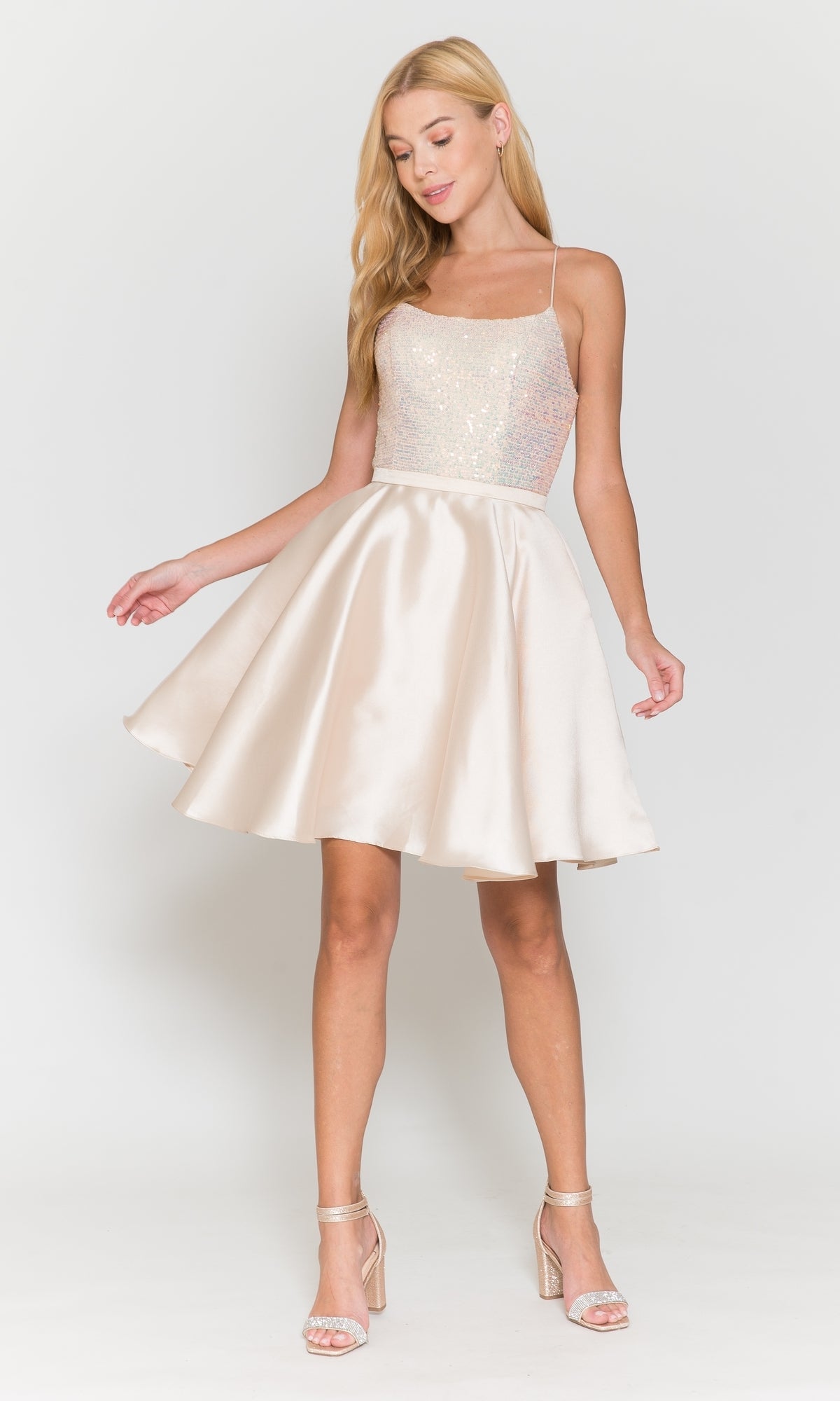 A woman wearing the Sequin-Bodice Short Flared Homecoming Dress 8730, a sleeveless, light-colored party dress with a sequined bodice, A-line silhouette, and flared satin skirt, paired with strappy high-heeled sandals.